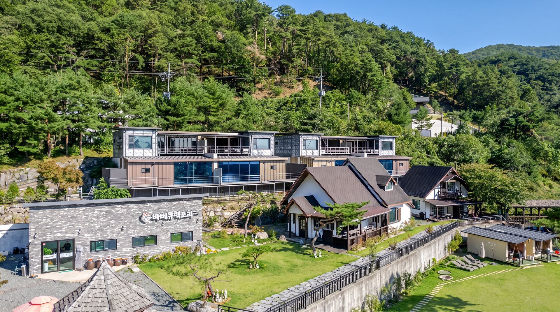 A modern two-story building with a flat roof, surrounded by a well-maintained garden and a stone wall.