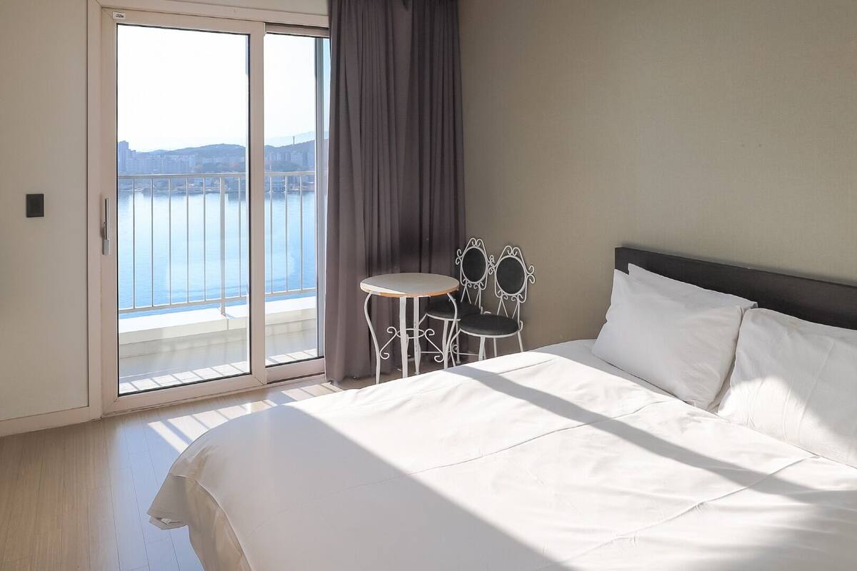 Habitación de hotel con una cama grande, una mesita con sillas y vistas a un cuerpo de agua a través de una puerta corredera.