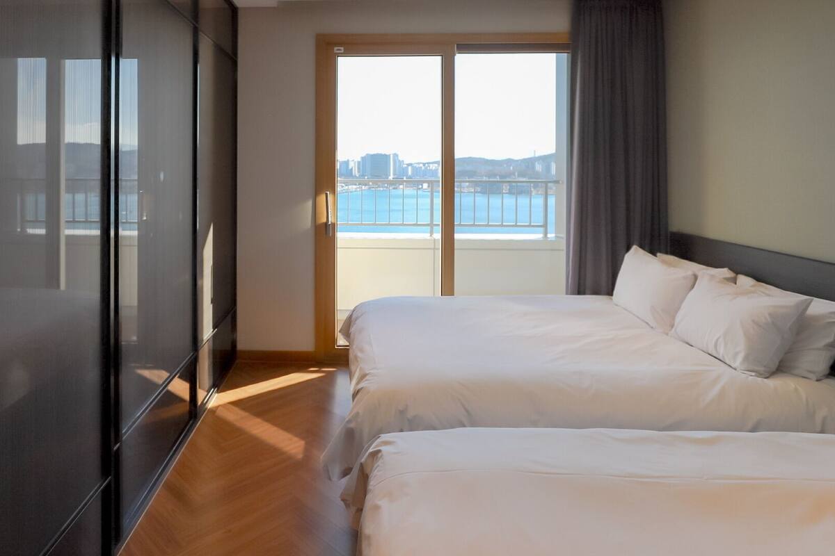 Habitación de hotel con dos camas, puerta corrediza al balcón y vista a la ciudad.