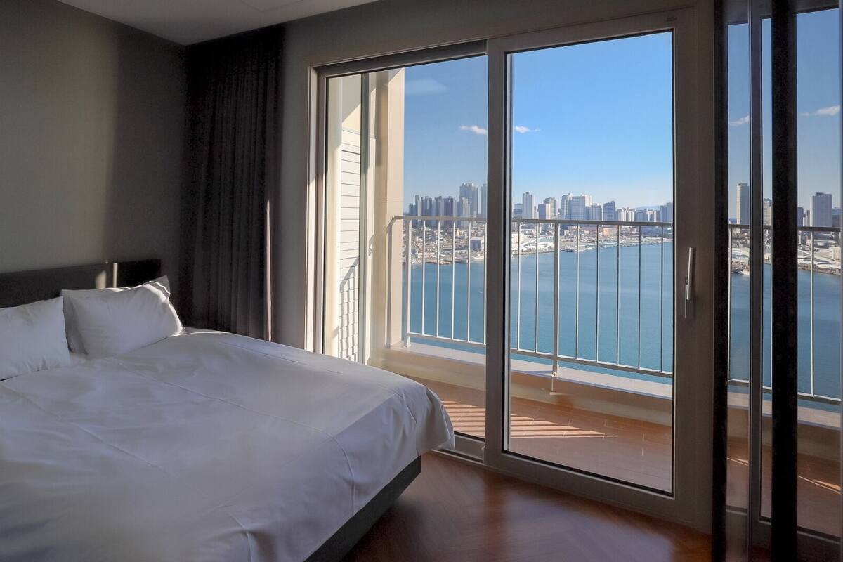 Una habitación de hotel con una cama grande, vistas a un horizonte urbano y un balcón con vista al agua.