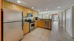 A kitchen with wooden cabinets, stainless steel appliances, and a tiled floor. - Free Beach Gear • Sparkling Clean • Best Value (Treasure Island)