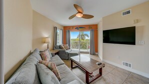 A living room with a sofa, a coffee table, a TV, and a ceiling fan. - Free Beach Gear • Sparkling Clean • Best Value (Treasure Island)
