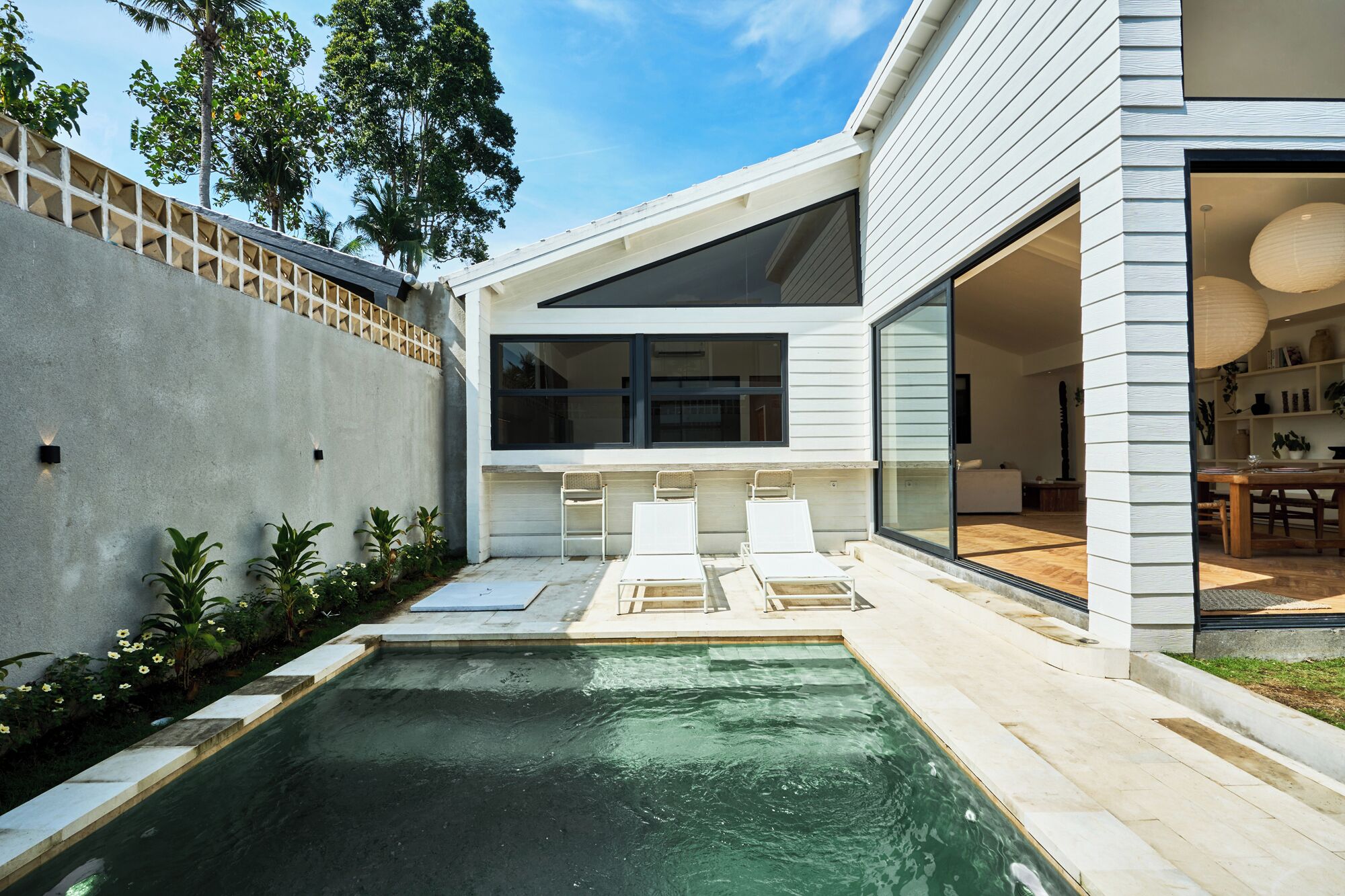 A modern house with a swimming pool, a covered outdoor seating area, and a large glass door leading to an interior space.