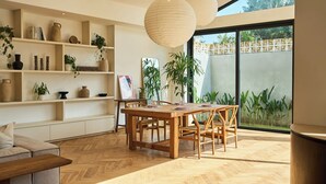 A spacious dining area with a wooden table and chairs, surrounded by shelves with decorative items and plants. - White Villa by Betterplace (Bengkel)