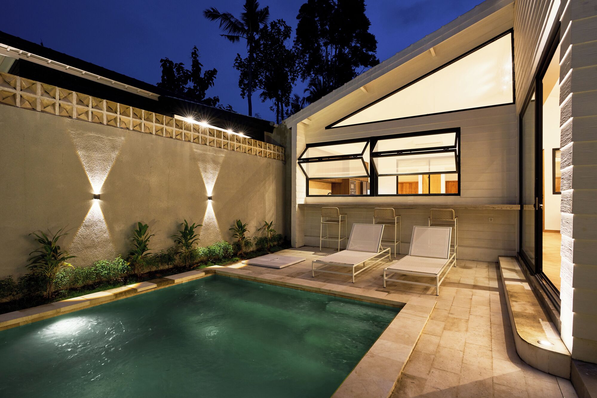 A modern pool area with a clear pool, lounge chairs, and a well-lit interior space.