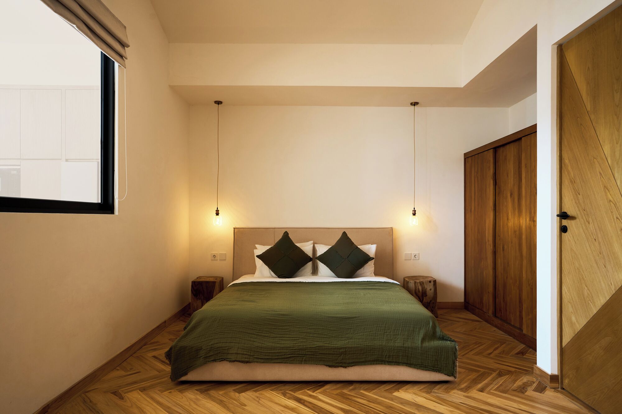 Un dormitorio con suelo de madera, una cama con manta verde, dos mesitas de noche y un armario de madera.