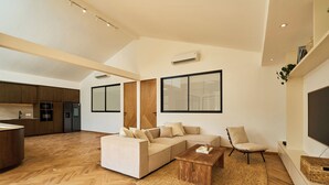 A modern living room with a sofa, coffee table, and a TV. There is a kitchen area with cabinets and appliances. - White Villa by Betterplace (Bengkel)