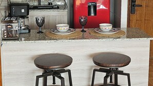 Une cuisine compacte avec une machine à café rouge, un four à micro-ondes et un grille-pain. Il y a deux tabourets au comptoir.