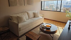Un salon moderne avec un canapé, une table basse et une vue sur la ville grâce à de grandes fenêtres.