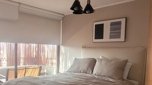 Une chambre à coucher avec un grand lit, un luminaire au plafond et une fenêtre avec des stores.