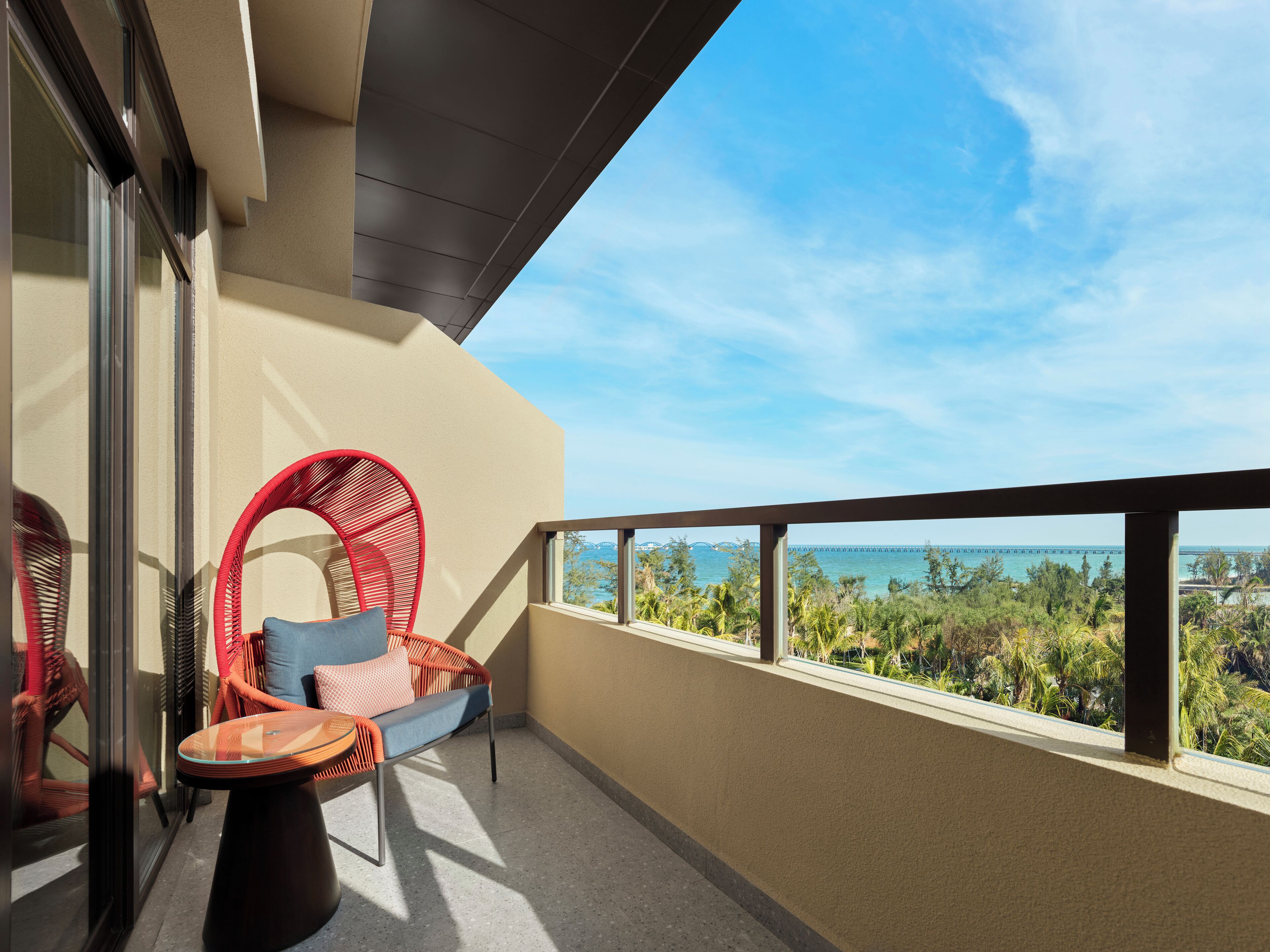 A balcony with a view of the sea, a red wicker chair, and a small table.