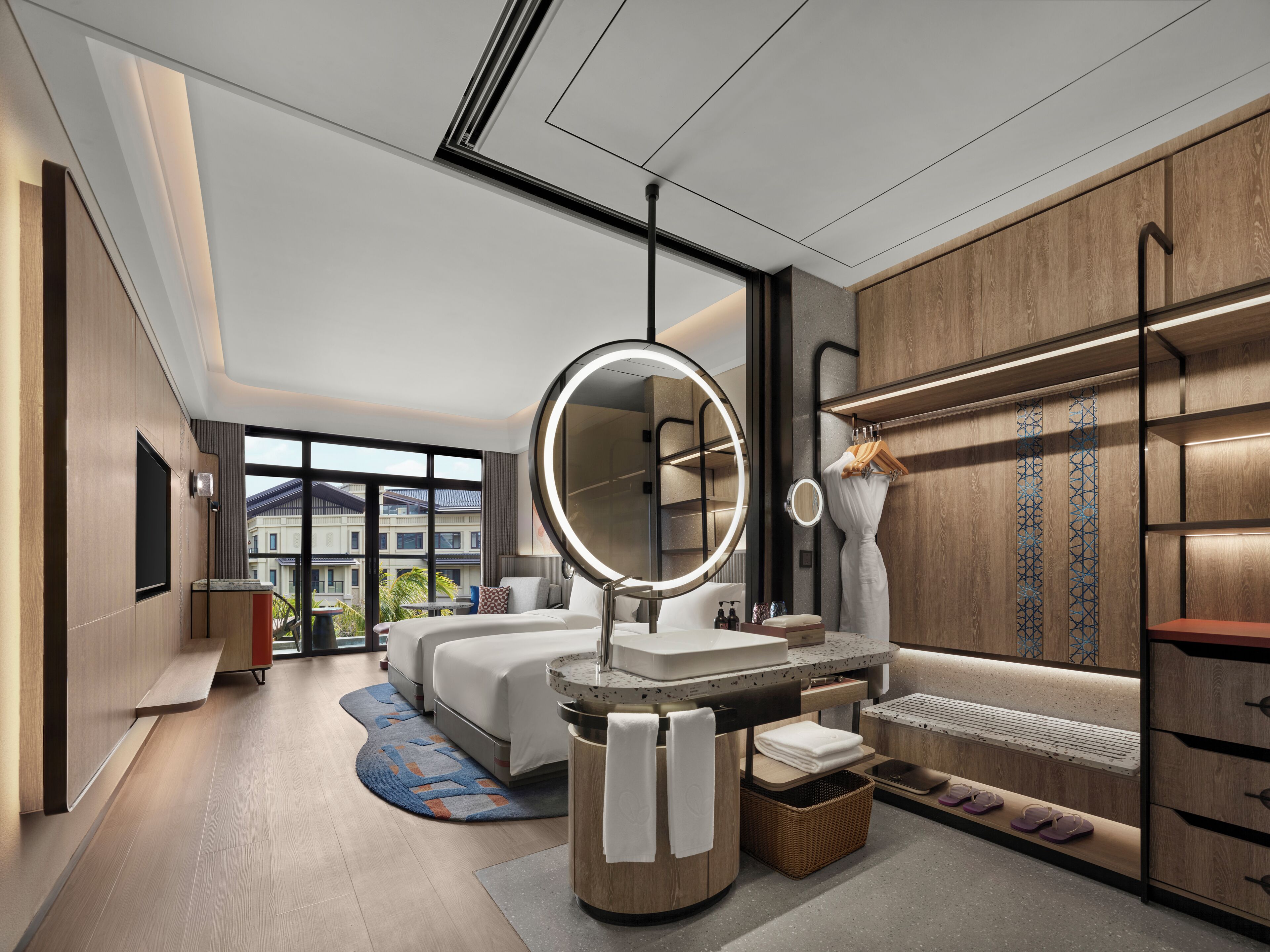 Une chambre d’hôtel moderne avec un grand lit, un miroir rond, une coiffeuse avec un lavabo et une vue sur la ville.