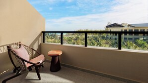 Un balcón con una silla de mimbre y una mesa redonda pequeña, con vistas a un edificio y follaje.
