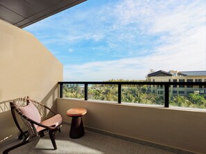 Un balcón con una silla de mimbre y una mesa redonda pequeña, con vistas a un edificio y follaje.