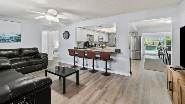 A modern living room with a black leather couch, a coffee table, and a bar area with stools. There is a kitchen in the background with a stainless steel refrigerator and a dining area with a pool view. - Spacious 4-bedroom house in wonderful Sarasota with AC (Sarasota)
