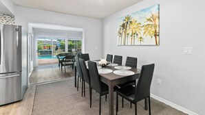 A modern kitchen with a stainless steel refrigerator, a dining area with a dark wooden table and black chairs, and a large window with a view of a swimming pool and greenery. - Spacious 4-bedroom house in wonderful Sarasota with AC (Sarasota)