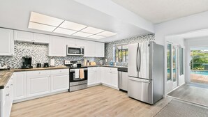 A modern kitchen with white cabinets, a stainless steel refrigerator, a microwave, and a tiled backsplash. - Spacious 4-bedroom house in wonderful Sarasota with AC (Sarasota)
