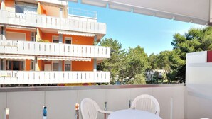 Een balkon met een ronde tafel en witte stoelen, met uitzicht op een gebouw met oranje en witte balkons.
