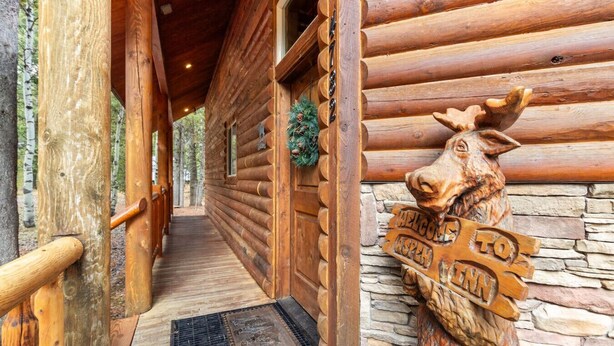 A wooden log cabin with a stone wall, a wooden door with a moose carving, and a welcome sign. - Aspen Inn just 20 minutes from Yellowstone National Park (Island Park)
