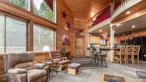 A cozy cabin interior with a plush armchair, a small table with a lamp, a sofa, a dining area with bar stools, and a kitchen with wooden cabinets and a black refrigerator. - Aspen Inn just 20 minutes from Yellowstone National Park (Island Park)
