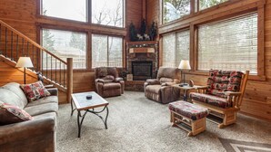 A cozy cabin interior with a fireplace, leather chairs, a sofa, and a wooden staircase. - Aspen Inn just 20 minutes from Yellowstone National Park (Island Park)