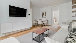Ein modernes Wohnzimmer mit Flachbildfernseher, Essbereich mit Stühlen und einer Couch mit gemusterten Kissen.