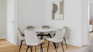 Ein Essbereich mit einem runden Tisch und sechs Stühlen, einem minimalistischen abstrakten Gemälde an der Wand und einer weißen Tür links.