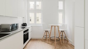 Eine moderne Küche mit weißen Schränken, einer Mikrowelle, einer Kaffeemaschine und einem Essbereich mit zwei weißen Stühlen und einem runden Tisch.