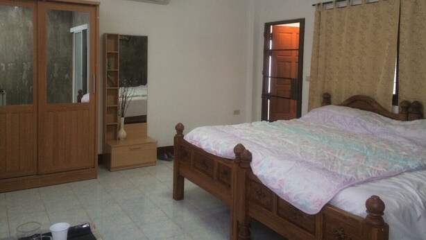 Ein Schlafzimmer mit einem hölzernen Bett, einem Kleiderschrank, einem Regal mit Dekoration und einem Fenster mit Vorhängen.