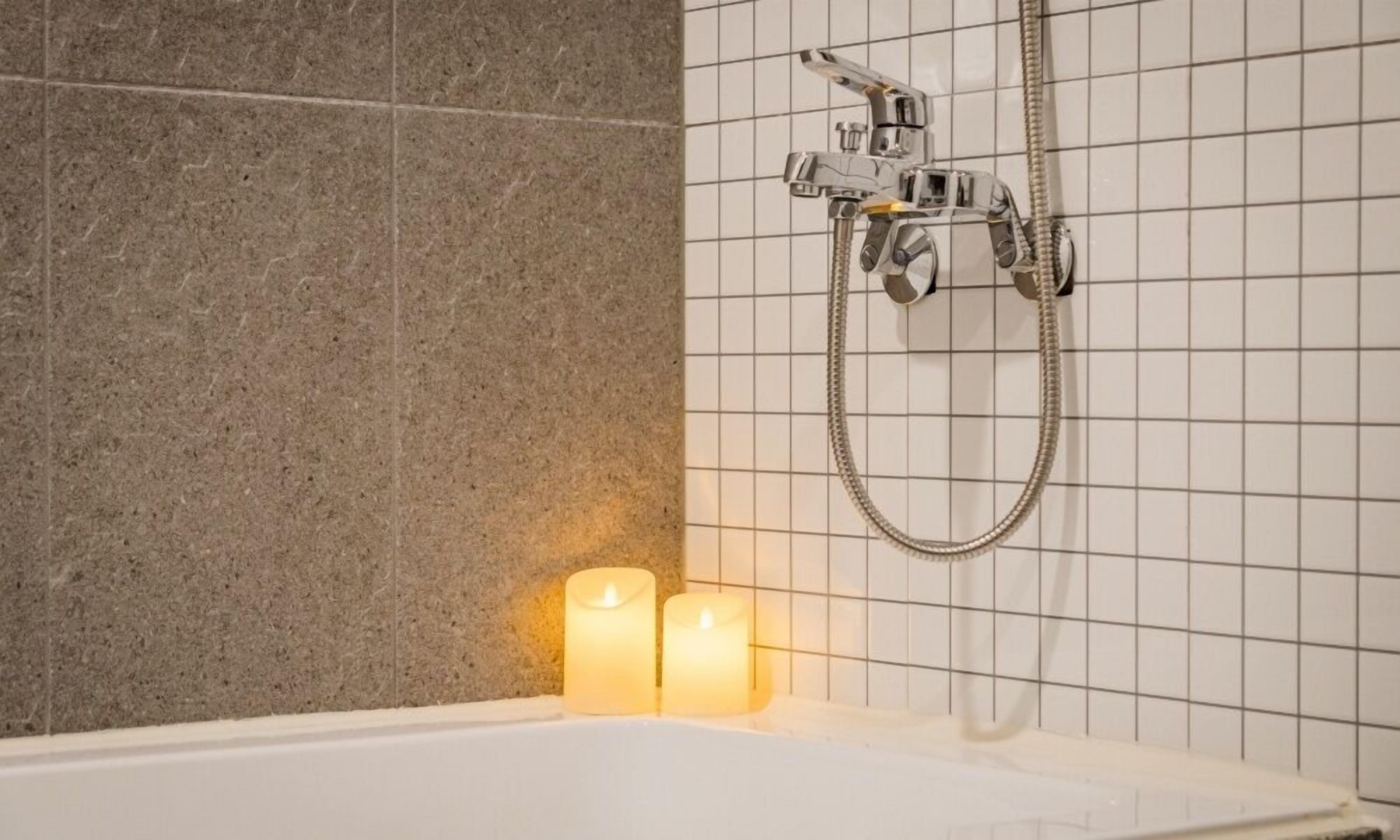 Un baño con bañera, ducha y dos velas encendidas.