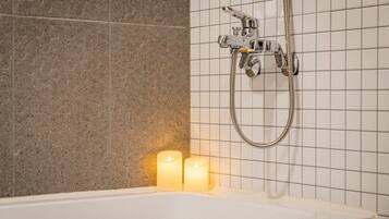 Un baño con bañera, ducha y dos velas encendidas.