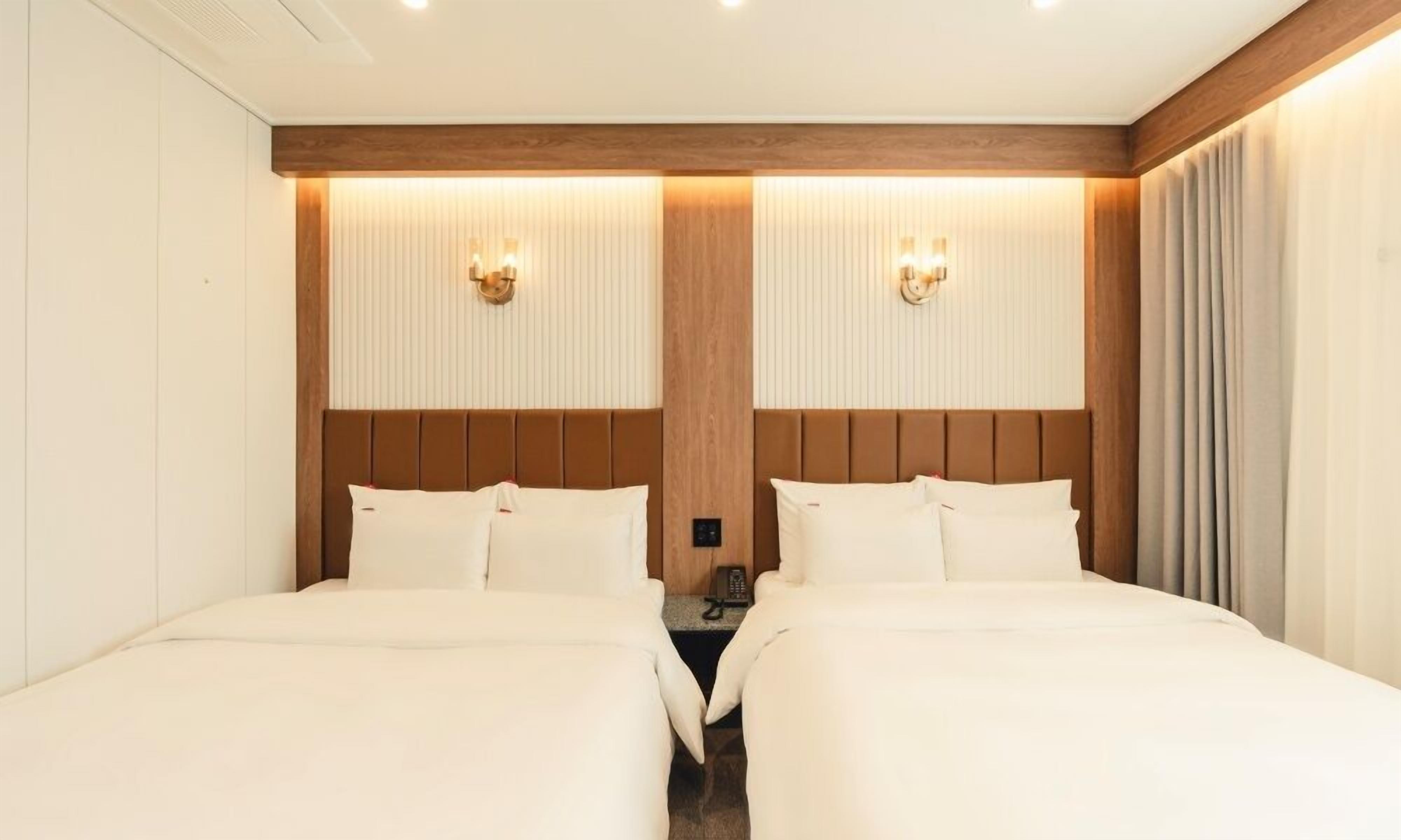 A hotel room with two beds, a wooden headboard, a nightstand, and a telephone.