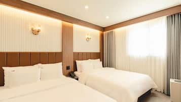 A hotel room with two beds, a wooden headboard, wall-mounted sconces, and a large window with curtains.