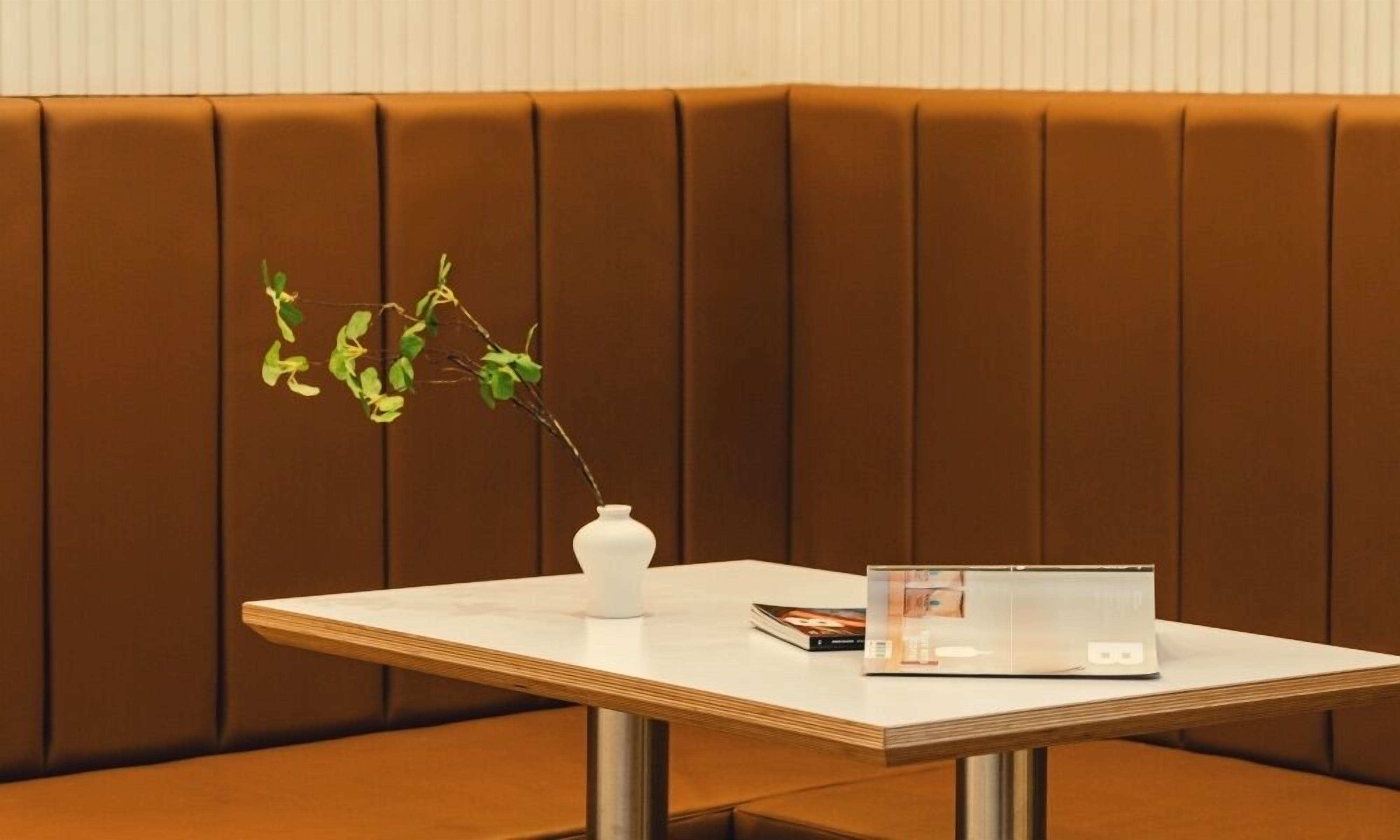 A corner booth with a white table, a white vase with a plant, and a laptop.