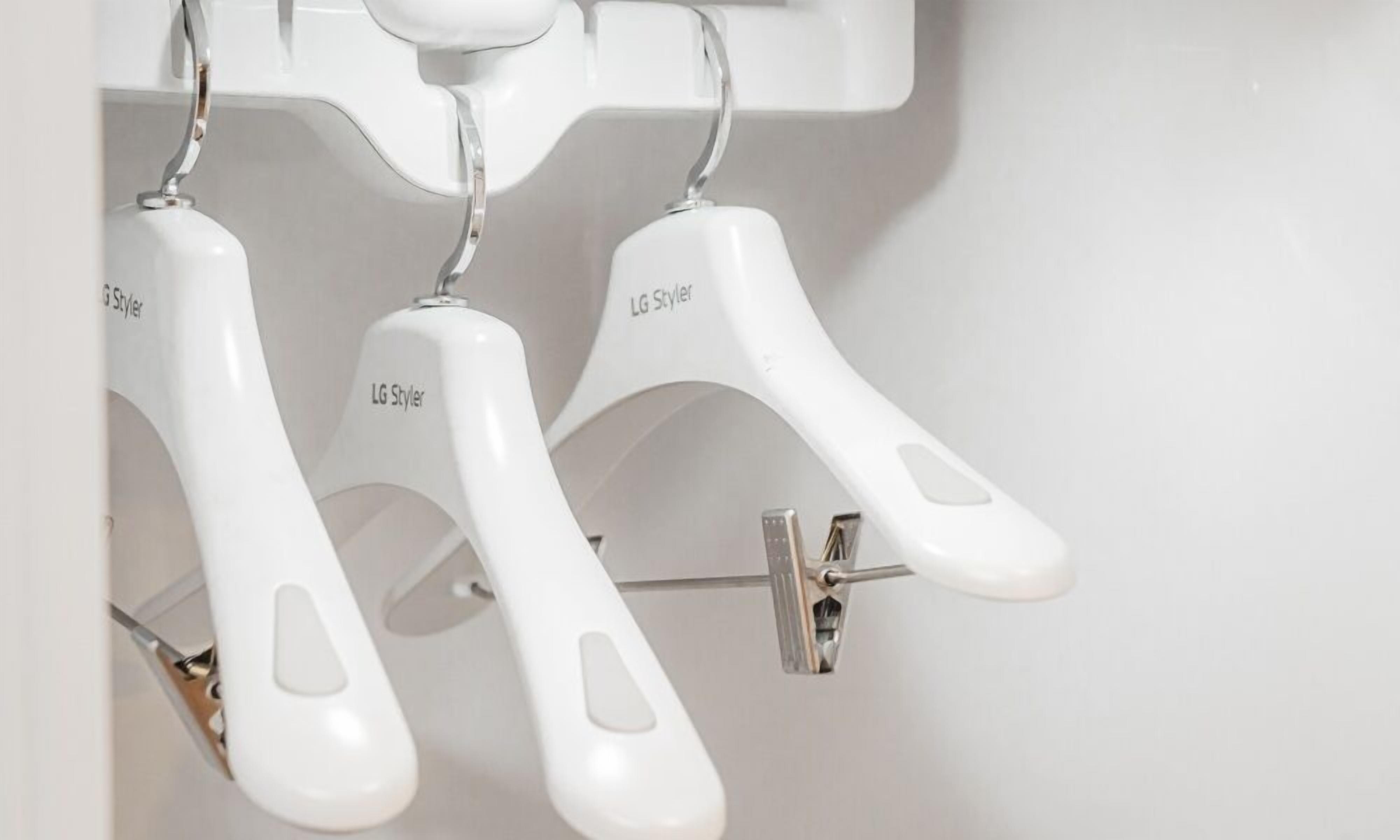 Three white LG Styler hangers hanging from a metal rod.