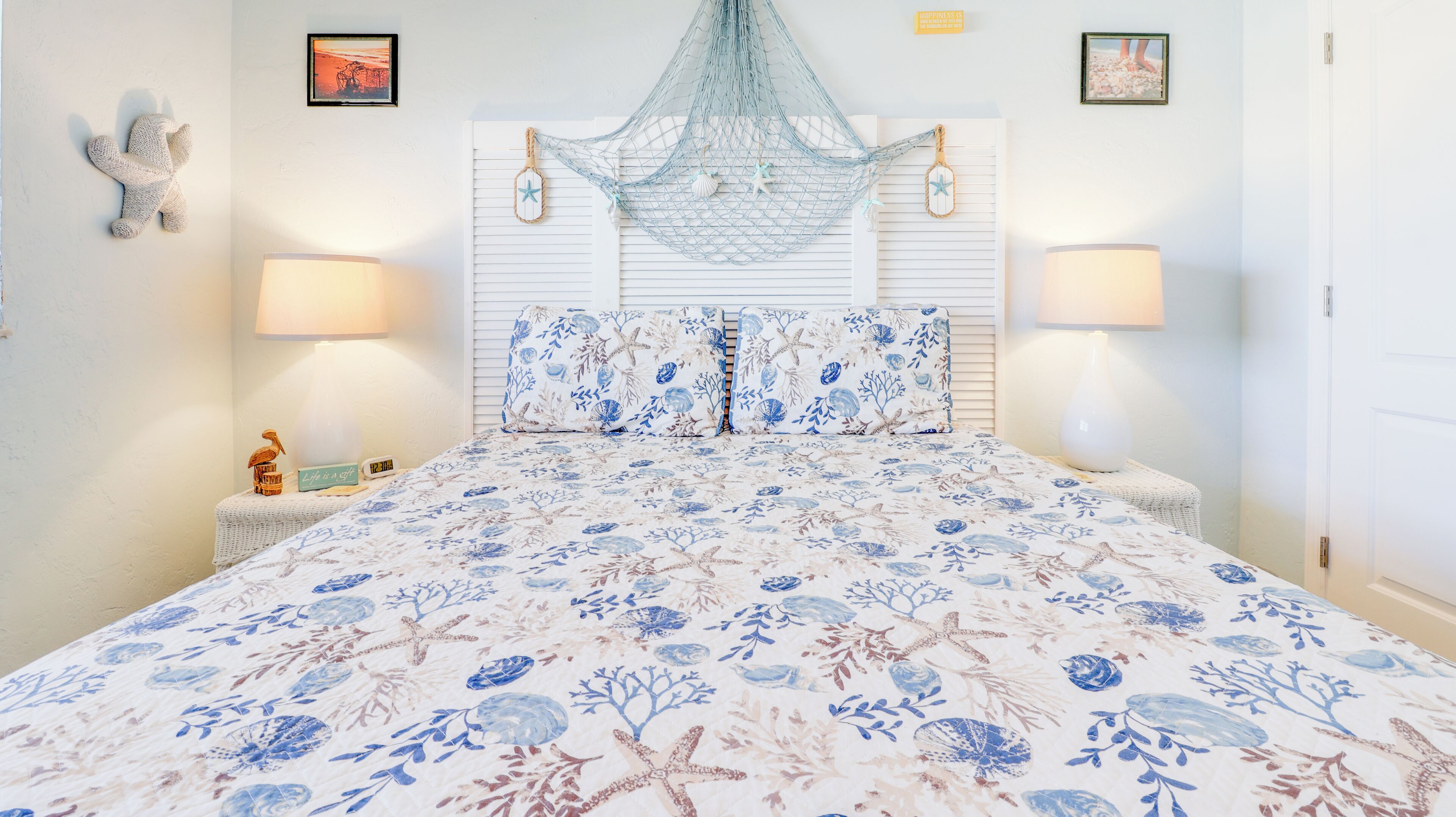 A bedroom with a floral bedspread, a hanging net, and two wall-mounted lamps.