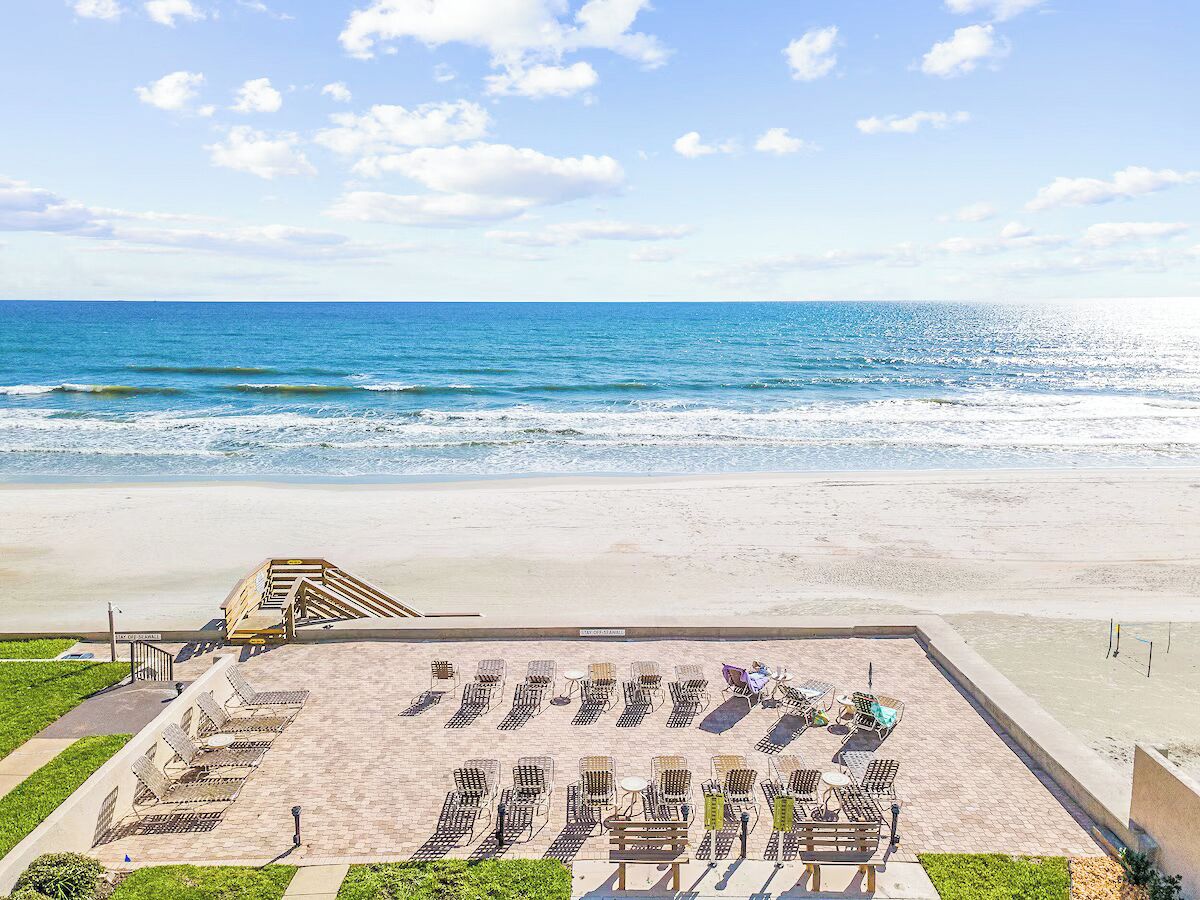 A beachside patio with sun loungers and tables, overlooking the ocean.