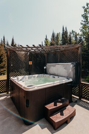 A hot tub with a wooden pergola and a step for access, surrounded by a lattice fence and trees. - Domaine à Ciel Ouvert (La Malbaie)