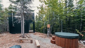A rustic cabin with a hot tub, wooden benches, and a covered area, surrounded by trees. - Domaine à Ciel Ouvert (La Malbaie)