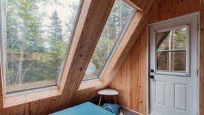 A room with a sloped ceiling, a bed, a door, and large windows offering a view of trees. - Domaine à Ciel Ouvert (La Malbaie)