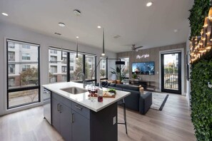 Une cuisine moderne dotée d’un grand îlot central, un coin repas avec un canapé et un salon équipé d’un téléviseur.