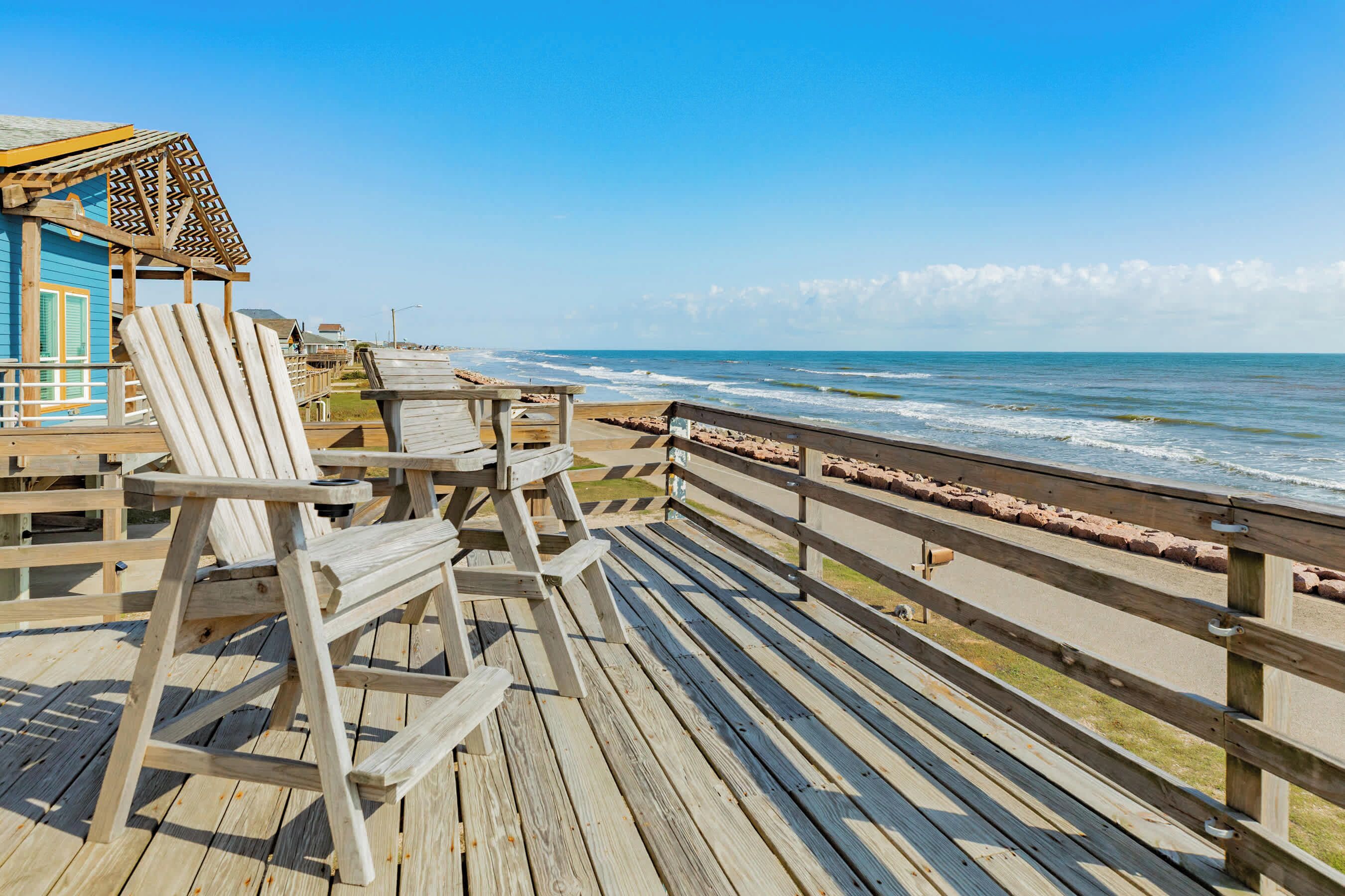 A wooden deck with chairs and a small building, overlooking the ocean.