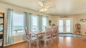 A dining area with a wooden table and chairs, a ceiling fan, and a view of the ocean through large windows. - Breakers Edge - Waterfront, 8 Sides of Sunshine! (Surfside Beach)