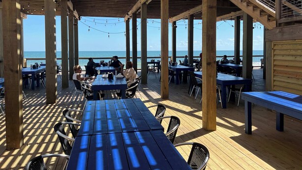 An outdoor dining area with wooden tables and chairs, overlooking the sea. - Breakers Edge - Waterfront, 8 Sides of Sunshine! (Surfside Beach)