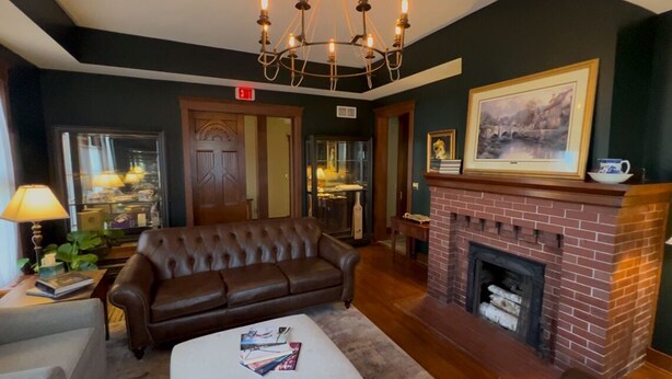 A cozy living room with a leather sofa, a fireplace, and a chandelier. - Charleston House Bed & Breakfast Inn (Charleston)