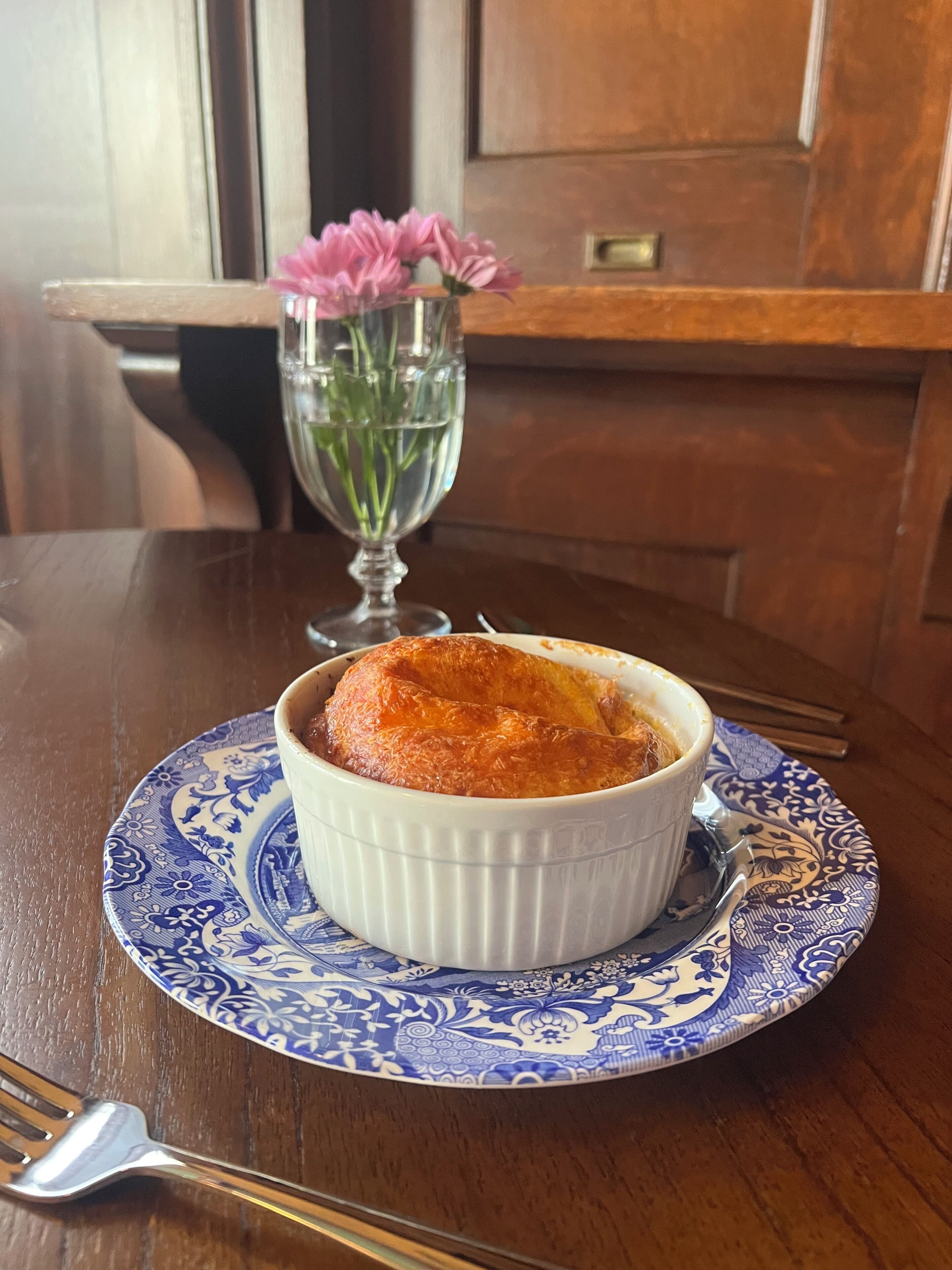 A dessert in a white ramekin on a blue and white patterned plate, with a fork beside it on a wooden table.