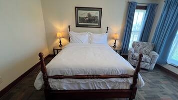 A hotel room with a large bed, two bedside tables with lamps, a chair, a framed picture on the wall, and a window with curtains.