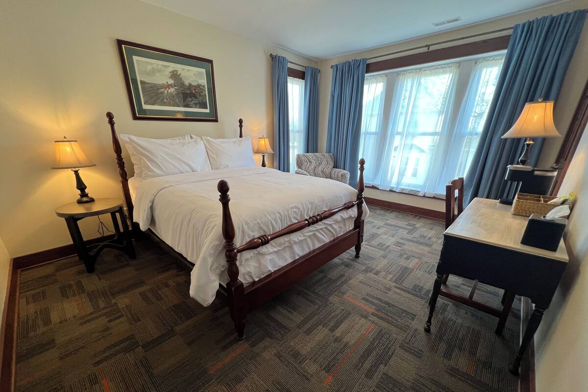 Una habitación de hotel ordenada con una cama, dos mesitas de noche, un escritorio y una silla.