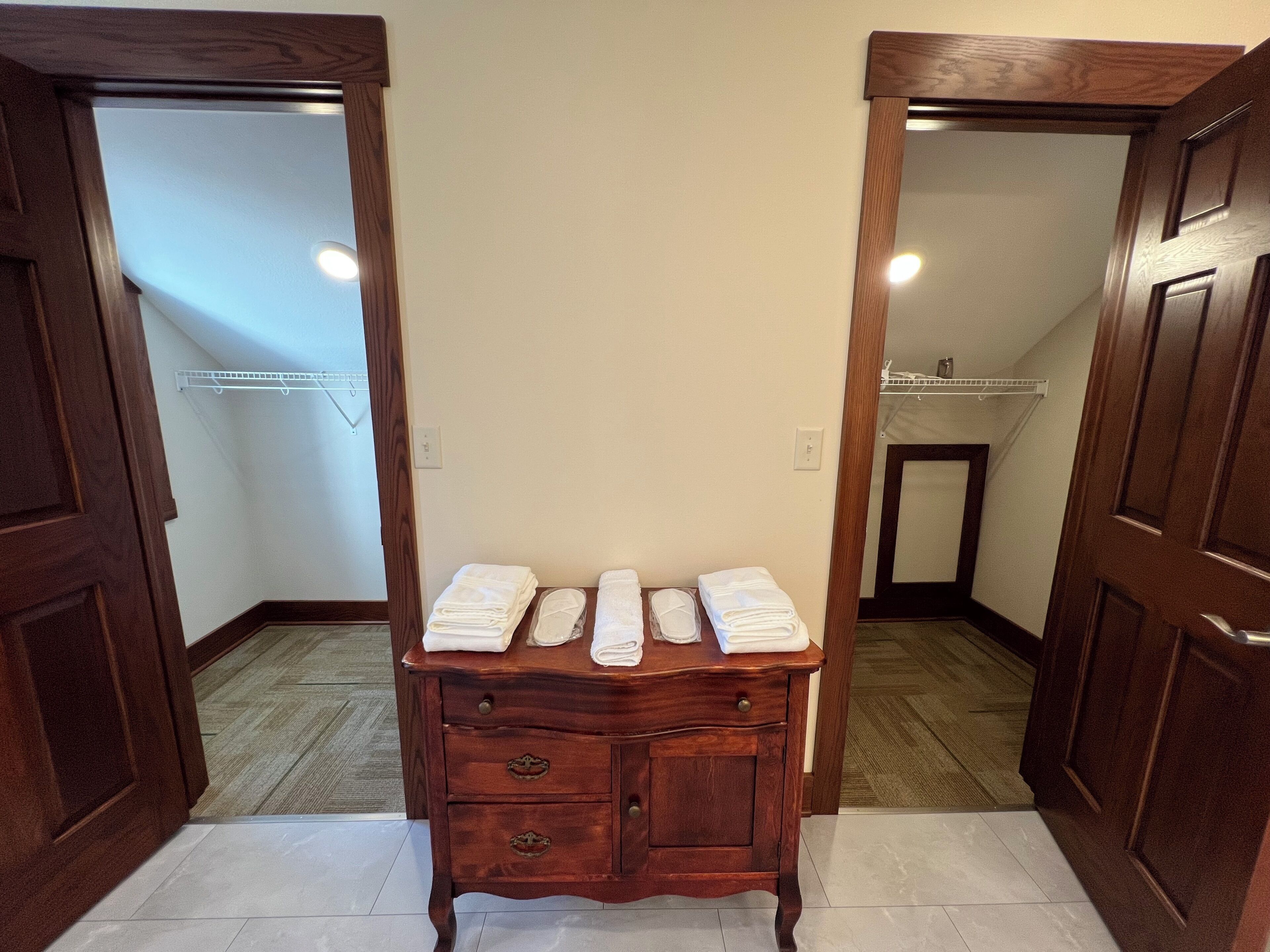 A hallway with wooden doors, a wooden dresser with folded white towels, and a tiled floor.