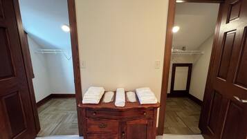 A hallway with wooden doors, a wooden dresser with folded white towels, and a tiled floor.